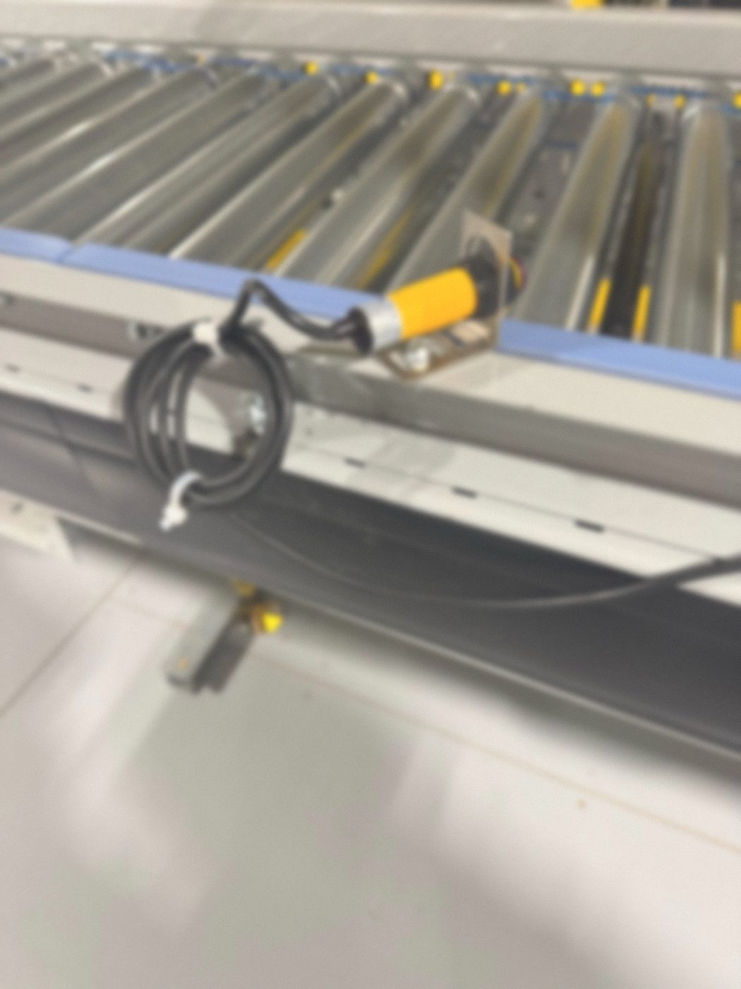 Photoelectric sensor on a mounting bracket with its cable secured on a roller conveyor